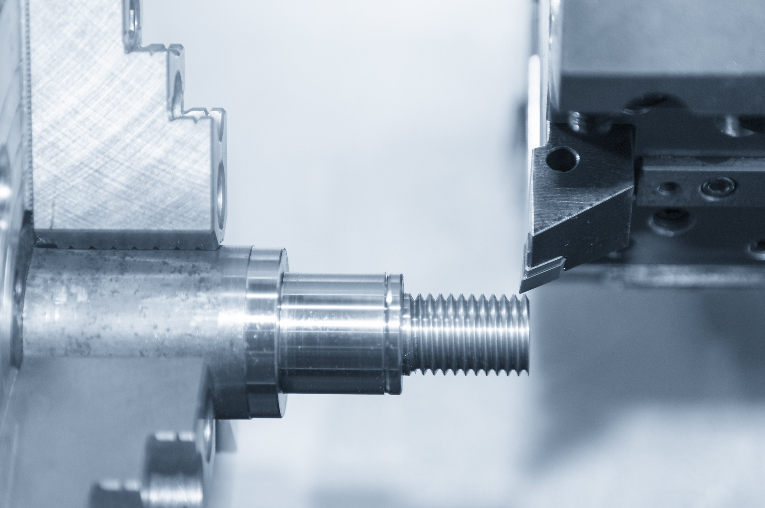 Thread Inspection: An Overview of the Most Popular Methods Closeup of the CNC lath machine (Turning machine) while cutting the screw thread in light blue scene.